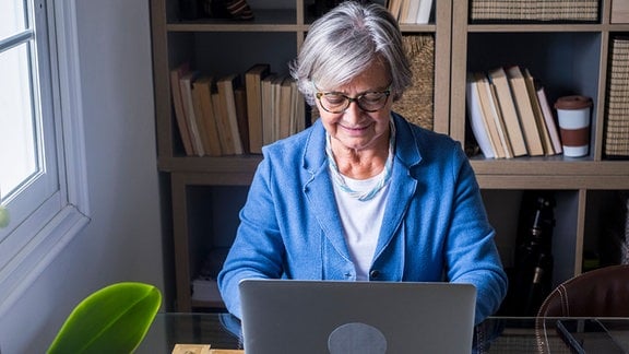 Lächelnde Unternehmerin arbeitet am Laptop vor Bücherregal zu Hause