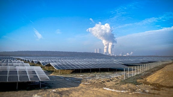 Blick von der Landstraße auf die Felder mit Photovoltaik-Modulen des Energieparks Witznitz im Süden von Leipzig. Im Hintergrund ist das Braunkohlekraftwerk Lippendorf zu sehen.