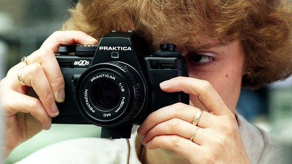 Eine Frau schaut durch den Sucher einer Praktica BX20 S Spiegelreflexkamera.