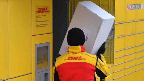 Ein DHL-Paketzsteller legt Paket in ein Fach einer Packstation.