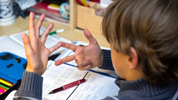 Ein Junge nimmt im Fach Mathematik seine Finger zur Hilfe