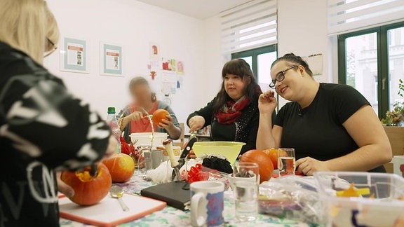 Frauen sitzen um einen Tisch und lachen, auf dem Tisch sind Kürbisse und Herbstdekoration.