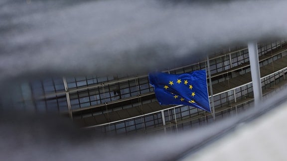 Die Flagge der Europäischen Union weht vor dem Gebäude des Europäischen Parlaments im Wind und spiegelt sich dabei in einer Pfütze vor dem Gebäude