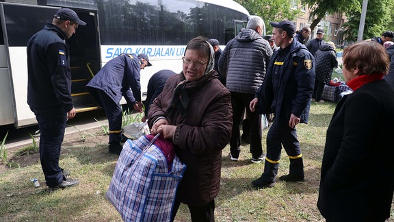 Eine ältere Frau trägt eine Tasche neben einem Bus, der in einem Zentrum für Menschen steht, die aus der Region Charkiw in Sicherheit gebracht wurden, in Charkiw im Nordosten der Ukraine.