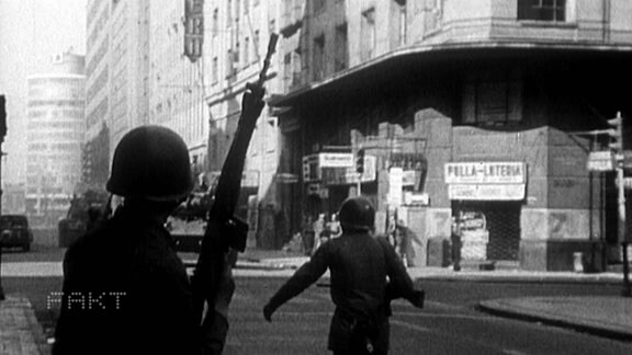 Ein Soldat steht mit erhobener Waffe auf einer STraße 