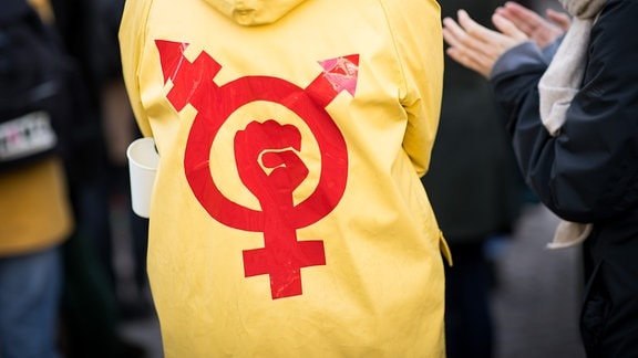  Eine Frau trägt einen gelben Regenmantel mit einem Gender- und Protestsymbol bei einer Kundgebung zum Internationalen Frauentag.