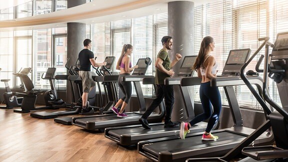 Zwei Frauen und zwei Männer trainieren in einem Fitnessstudio auf Laufbändern.
