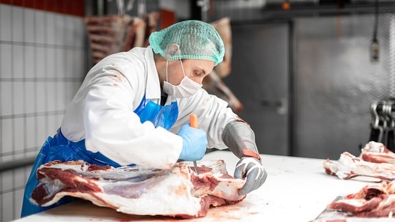 Ein Mitarbeiter eines Schlachthofes zerteilt ein Fleischstück