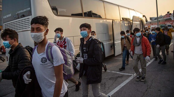 Eine Gruppe unbegleiteter Kinder aus überfüllten griechischen Flüchtlingslagern tragen Schutzmasken, nachdem sie mit einer Fähre im Hafen von Piräus angekommen sind und nun zu einem Bus gehen.