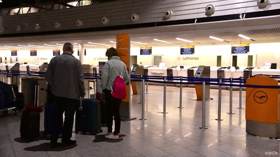 Fluggäste stehen mit ihrem Gepäck in der Abflughalle eines Flughafens