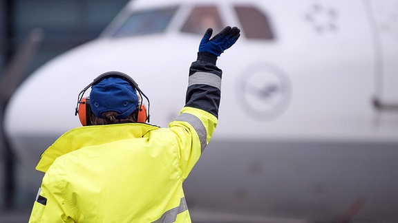 Eine Mitarbeiterin des Bodenpersonals winkt am Frankfurter Flughafen einer Lufthansa-Maschine auf dem Rollfeld zu