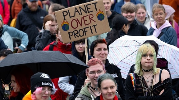 Zahlreiche Menschen nehmen an einer Demonstration zum Klimastreik teil und halten ein Plakat mit der Aufschrift „Planet over profit“ in die Höhe