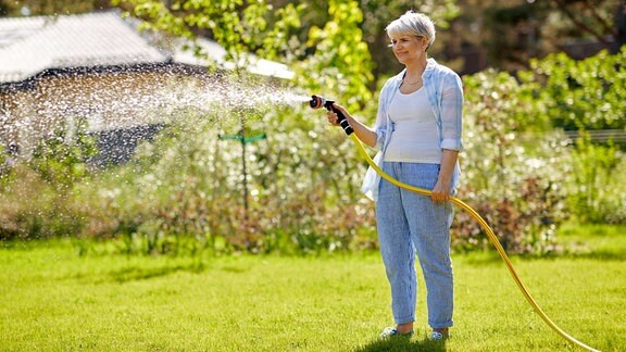 Eine Frau bewässert den Rasen ihres Gartens.