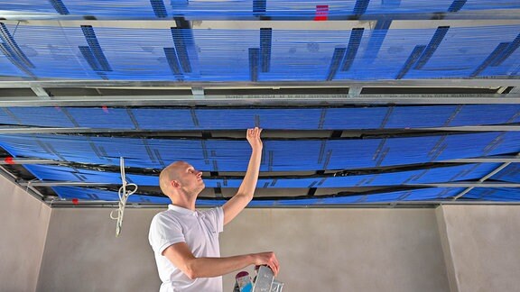 Ein Mann installiert an einer Decke Kapillarrohrmatten, die als Flächenheizung und -kühlung eingesetzt werden