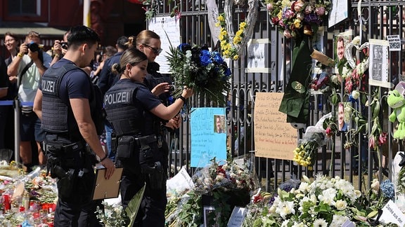 Polizisten an einem zum Gedenken an einen getöteten Kollegen mit Blumen und Bildern geschmückten Zaun