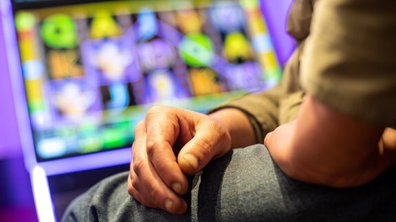 Ein Mann sitzt vor einem Glücksspielautomaten. 
