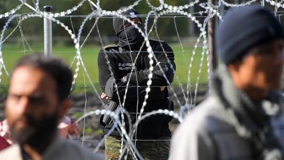 Polnischer Grenzwächter schaut auf Flüchtlingscamp hinter Grenzzaun.