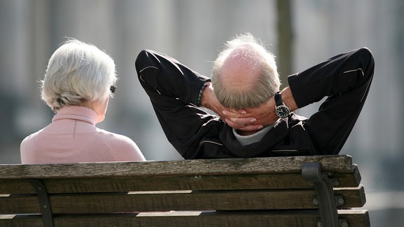 Ein Rentnerpaar sitzt auf einer Bank und sonnt sich