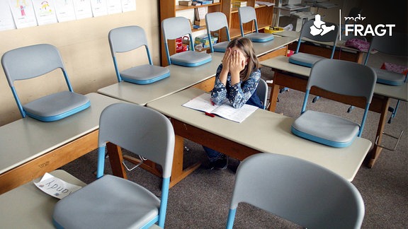 Eine Schuelerin sitzt alleine in einem Klassenraum.