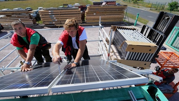 Monteure bringen Photovoltaikmodule an einem Gebäude an