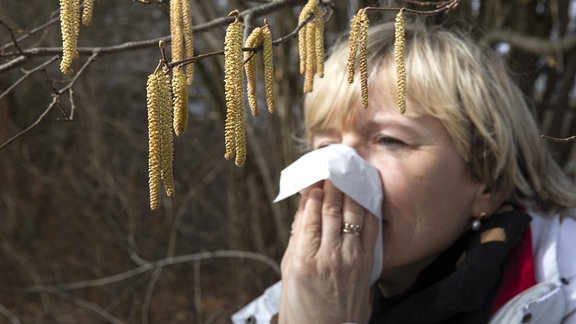 Eine Frau steht unter einem Haselstrauch und putzt sich die Nase