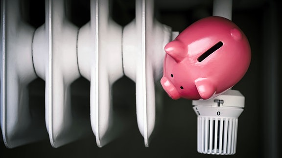 Ein Sparschwein auf der Heizung, deren Thermostat auf Null steht.