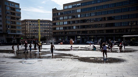 Kinder spielen an Wasserfontänen.