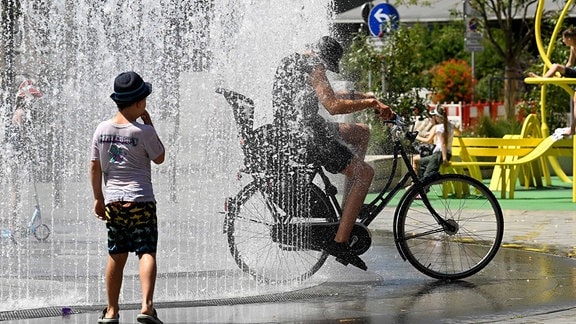 Ein Radfahrer fährt bei den heissen Temperaturen direkt durch einen Springbrunnen