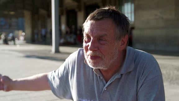 Ein Mann mit grauem T-Shirt sitzt in der Sonne vor dem Hauptbahnhof in Leipzig