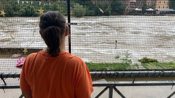 Eine Frau steht auf einem Balkon und schaut auf Hochwasser vor ihrer Wohnung.