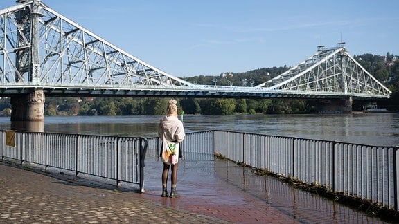 Eine Passantin steht am Ufer der Hochwasser führenden Elbe vor der Elbbrücke Blaues Wunder.