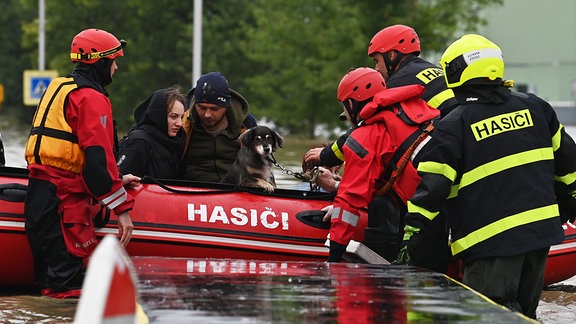 Feuerwehrleute evakuieren Menschen und einen Hund aus einem überfluteten Gebiet