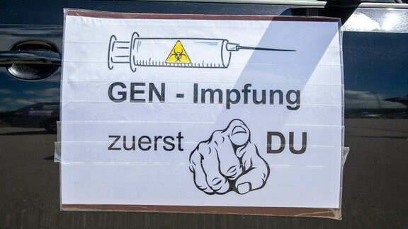 Querdenker veranstalten Autokorso, Schild: Gen- Impfung zuerst du.