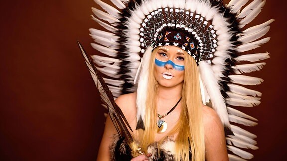 Frau als Indianerin kostümiert mit großem Federschmuck auf dem Kopf.