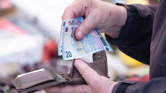 Eine Frau sortiert auf einem Wochenmarkt das Wechselgeld für ihre Einkäufe in ein Portemonnaie