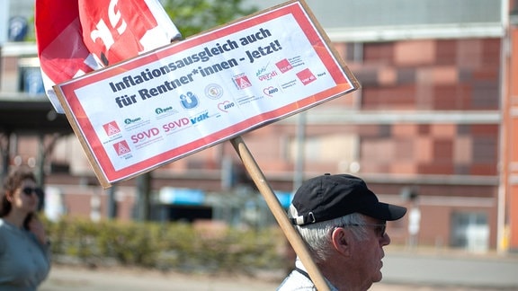 Ein Demonstrant mit einem Transparent mit der Aufschrift Inflationsausgleich auch für Rentner*innen - Jetzt!