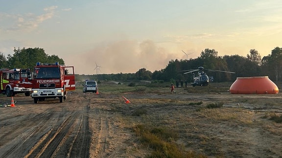 Feuerwehrkräfte sind neben einem Löschhubschrauber in einem Waldstück nahe Jüterbog im Einsatz