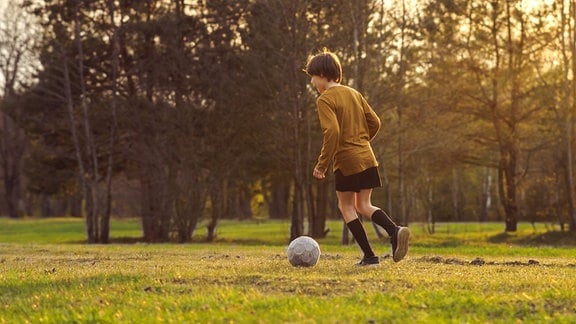 Ein Junge spielt auf einer Wiese Fußball