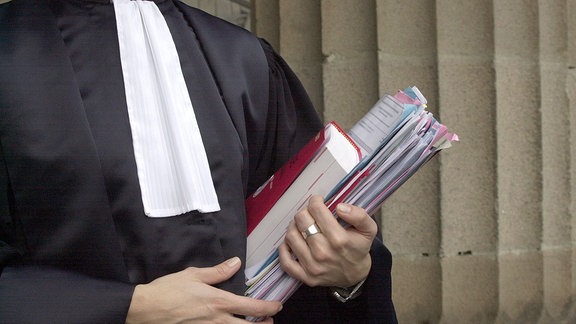 Eine Person in einer Richterrobe hält Akten und Gesetzbuch in der Hand