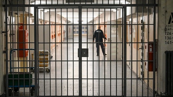 Ein Vollzugsbeamter öffnet eine Zellentür in einem mit Gittern gesicherten Zellengang.