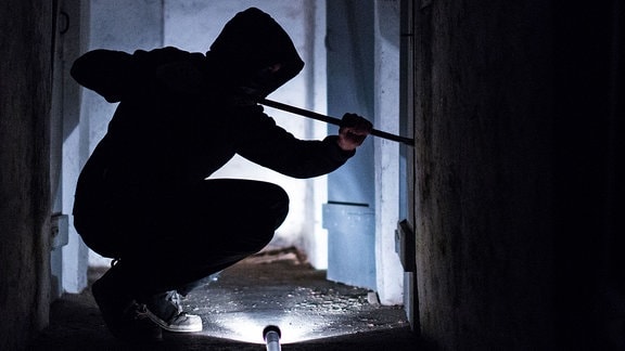 Ein Mann hantiert mit einem Brecheisen an einer Kellertür
