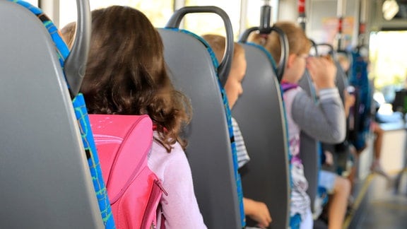 Kinder sitzen mit ihrem Ranzen in einem Schulbus.
