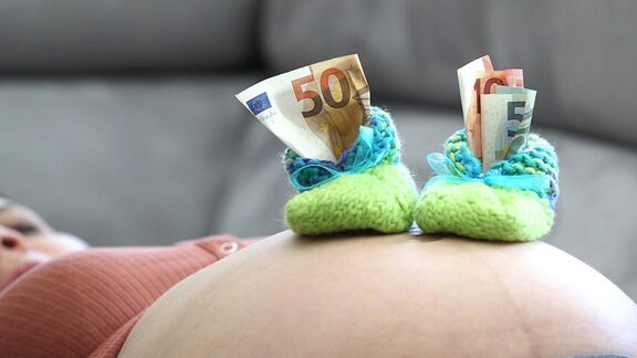Babyschühchen mit Geld auf einem Schwangerschaftsbauch