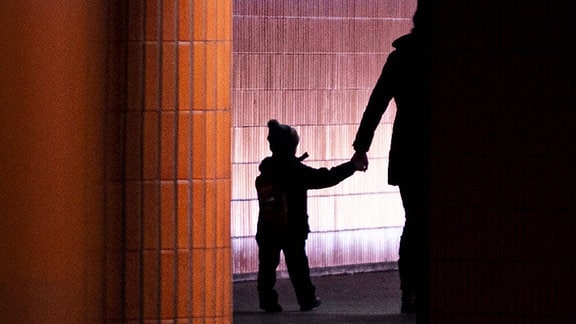 Die Silhouette eines Kindes an der Hand eines Erwachsenen