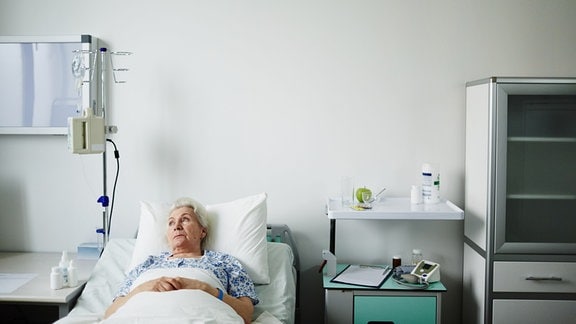 Eine Patientin liegt im Krankenhausbett und blickt aus dem Fenster.