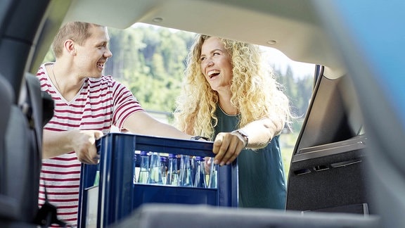 Ein Paar stellt ein Kasten Wasser in den Kofferraum eines Autos.