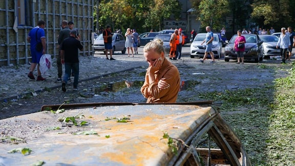 Eine junge Frau neben einem bei einem Angriff beschädigten Pkw