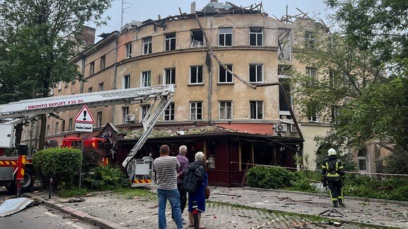 Menschen beobachten einen Feuerwehreinsatz nach einem Raketenangriff, bei dem ein Gebäude beschädigt wurde.