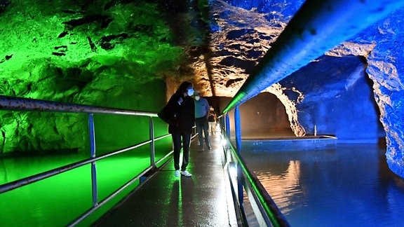 Besucher der Marienglashöhle laufen auf einem Steg in der farbig beleuchteten Höhle
