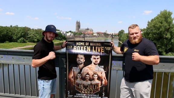 Zwei Boxer posieren mit Plakat am Geländer einer Elbbrücke in Magdeburg.